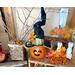 A fall table Halloween table display. There is a pumpkin witch, a vase that holds tree branches, all leaves, and orange berries.